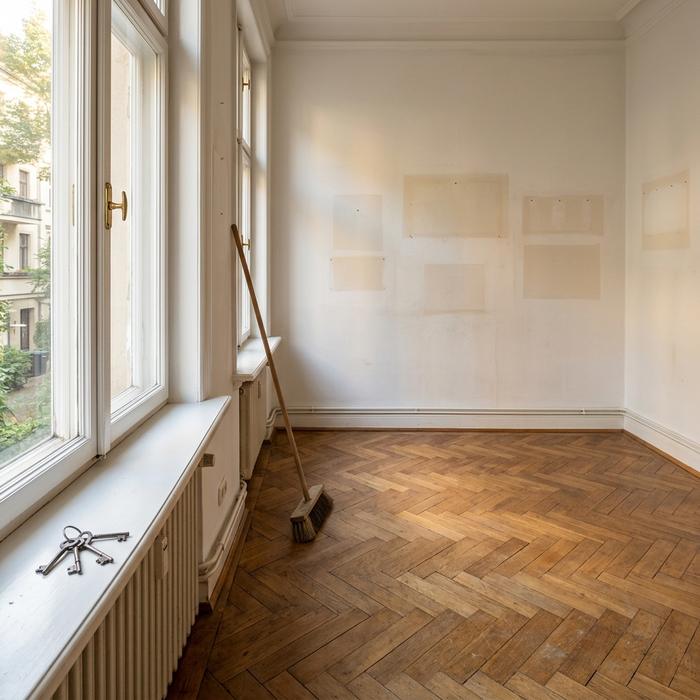 Leer geräumtes, gefegtes Zimmer mit Parkett, Besen und Schlüsselbund auf der Fensterbank